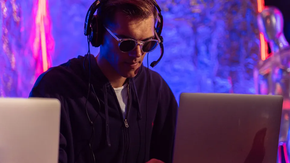 Man wearing headphones working on a laptop in a room lit with neon light
